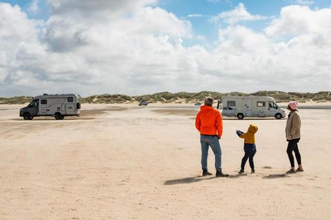 Gunnar Herbst lässt mit seinem Sohn und seiner Frau am Strand einen Drachen steigen, im Hintergrund Wohnmobile