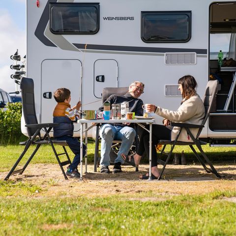 Redakteur Gunnar Herbst, seine Frau und ihr Sohn sitzen an einem Campingtisch vor ihrem Wohnmobil und essen