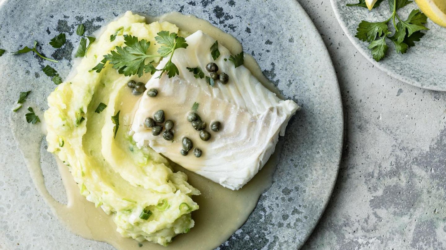 Auf blauen Tellern sind Kabeljau mit Kapernsauce und Kartoffelpüree, und Zitronenspalten zu sehen