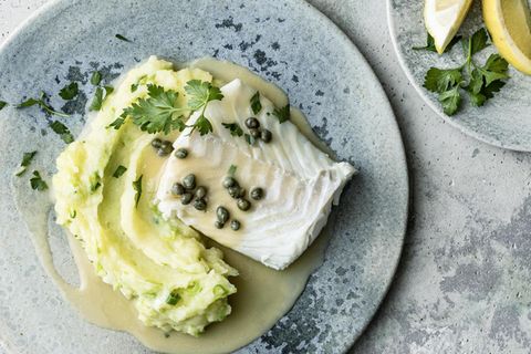 Auf blauen Tellern sind Kabeljau mit Kapernsauce und Kartoffelpüree, und Zitronenspalten zu sehen