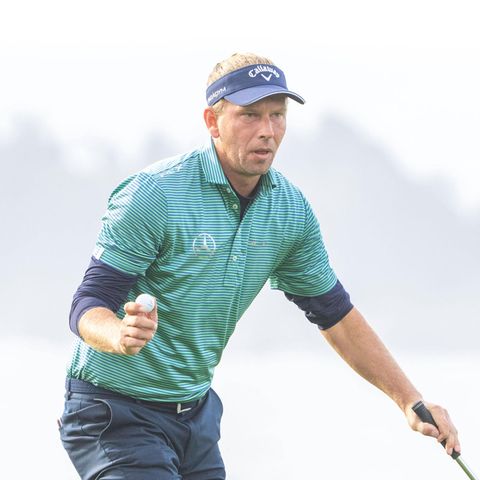 Marcel Siem trägt eine Schirmmütze und hält einen Golfball in der Hand