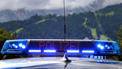 Vor einer bergigen grünen Landschaft leuchten Blaulicht und "Polizei"-Schriftzug eines Polizeiwagens