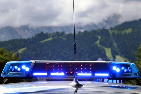 Vor einer bergigen grünen Landschaft leuchten Blaulicht und "Polizei"-Schriftzug eines Polizeiwagens