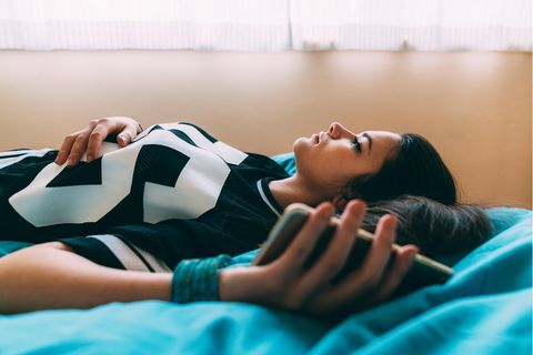 Eine Frau liegt auf dem Bett und hat ihr Smartphone in der Hand.
