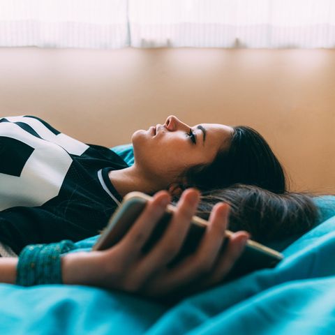 Eine Frau liegt auf dem Bett und hat ihr Smartphone in der Hand.