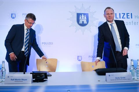 Polizeipräsident Martin Meyer und Innensenator Andy Grote setzen sich an einen Tisch unter dem Wappen der Polizei Hamburg