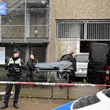 Zwei Bestatter rollen eine Bahre mit schwarzem Leichensack darauf zu ihrem Transporter