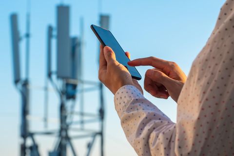 Frau steht mit einem Handy vor einem Sendemast
