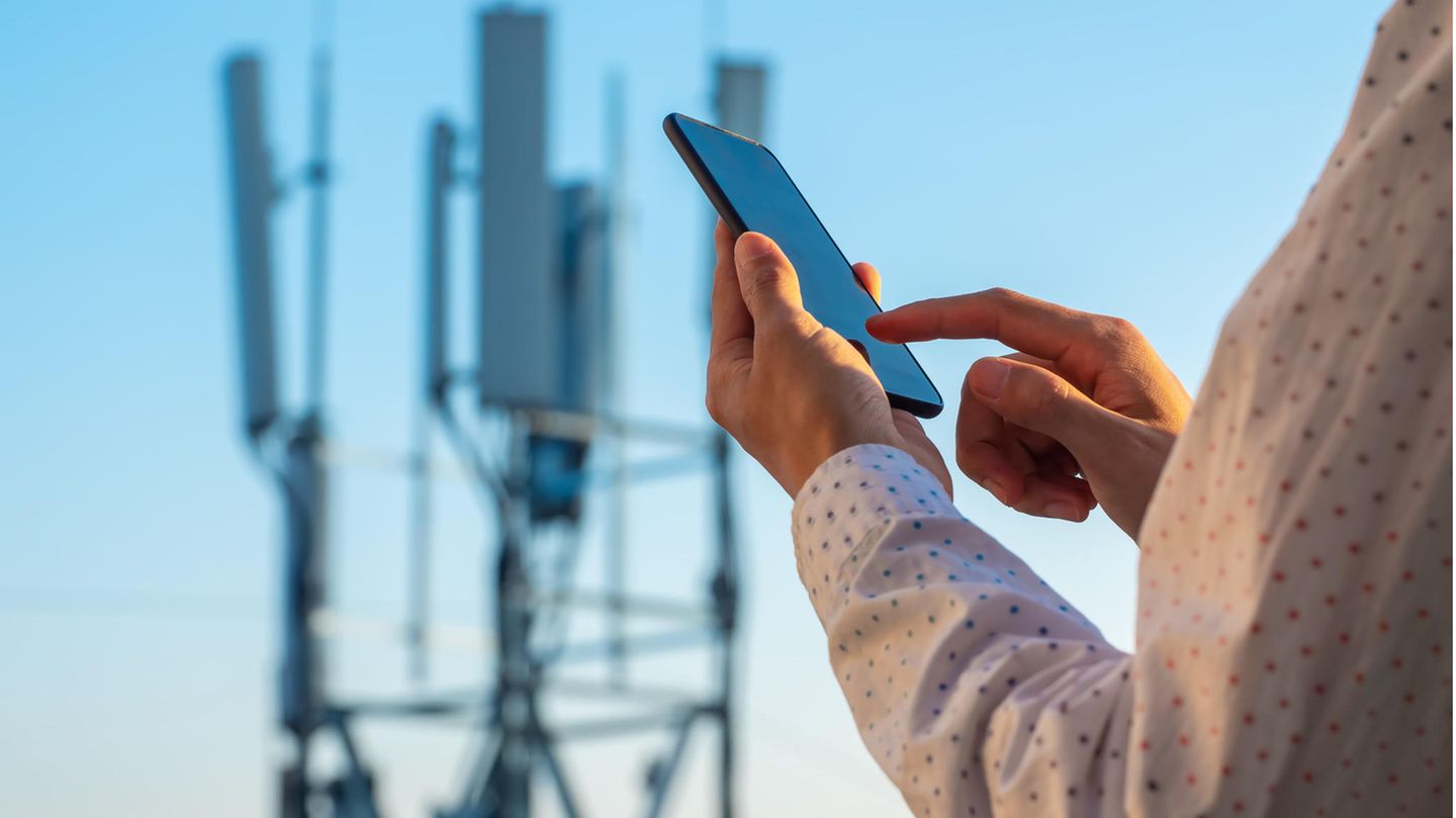 Frau steht mit einem Handy vor einem Sendemast