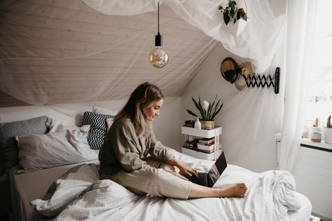 Frau sitzt mit Laptop auf einem Bett