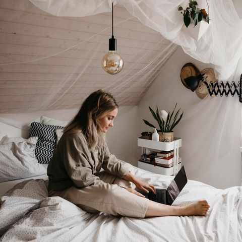 Frau sitzt mit Laptop auf einem Bett