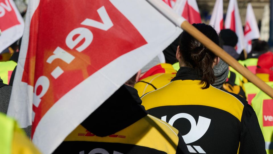 Menschen in Post-Jacken tragen Flaggen der Gewerkschaft Verdi