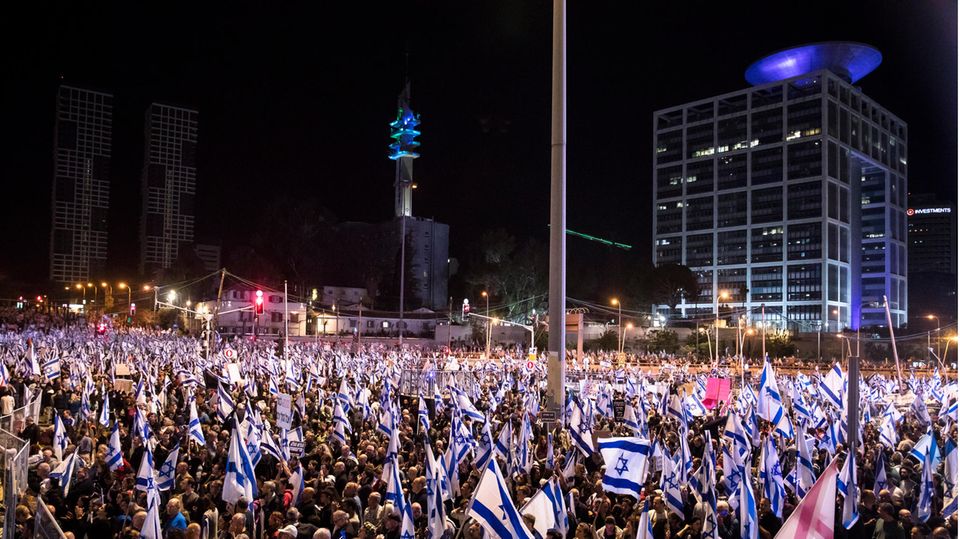Im Dunkeln steht eine Menschenmenge mit vielen israelischen Flaggen auf einem Platz