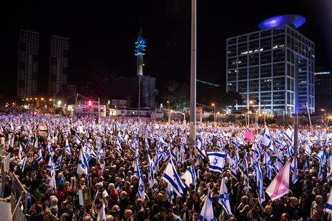 Im Dunkeln steht eine Menschenmenge mit vielen israelischen Flaggen auf einem Platz