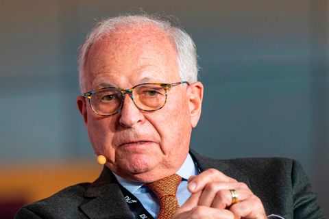 Wolfgang Ischinger sitzt in Anzug und Krawatte auf einem Podium und spricht, während er mit beiden Händen gestikuliert