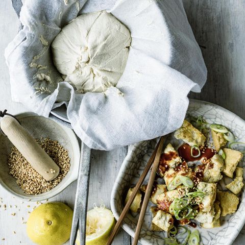 In drei hellen Schalen sind Sesamkörner, ein Mulltuch mit selbstgemachter Tofumasse, und fertiger Tofu mit einer Sauce