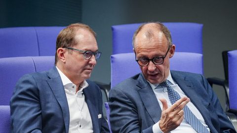 Alexander Dobrindt und Friedrich Merz sitzen in Anzügen auf blau gepolsterten Stühlen im Bundestag nebeneinander und diskutieren