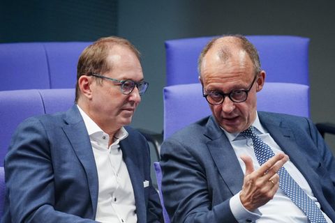 Alexander Dobrindt und Friedrich Merz sitzen in Anzügen auf blau gepolsterten Stühlen im Bundestag nebeneinander und diskutieren