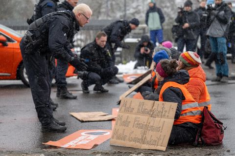 Polizisten reden mit Aktivistinnen der Letzten Generation, die sich auf der Fahrbahn der Jahnallee in Leipzig festgeklebt haben