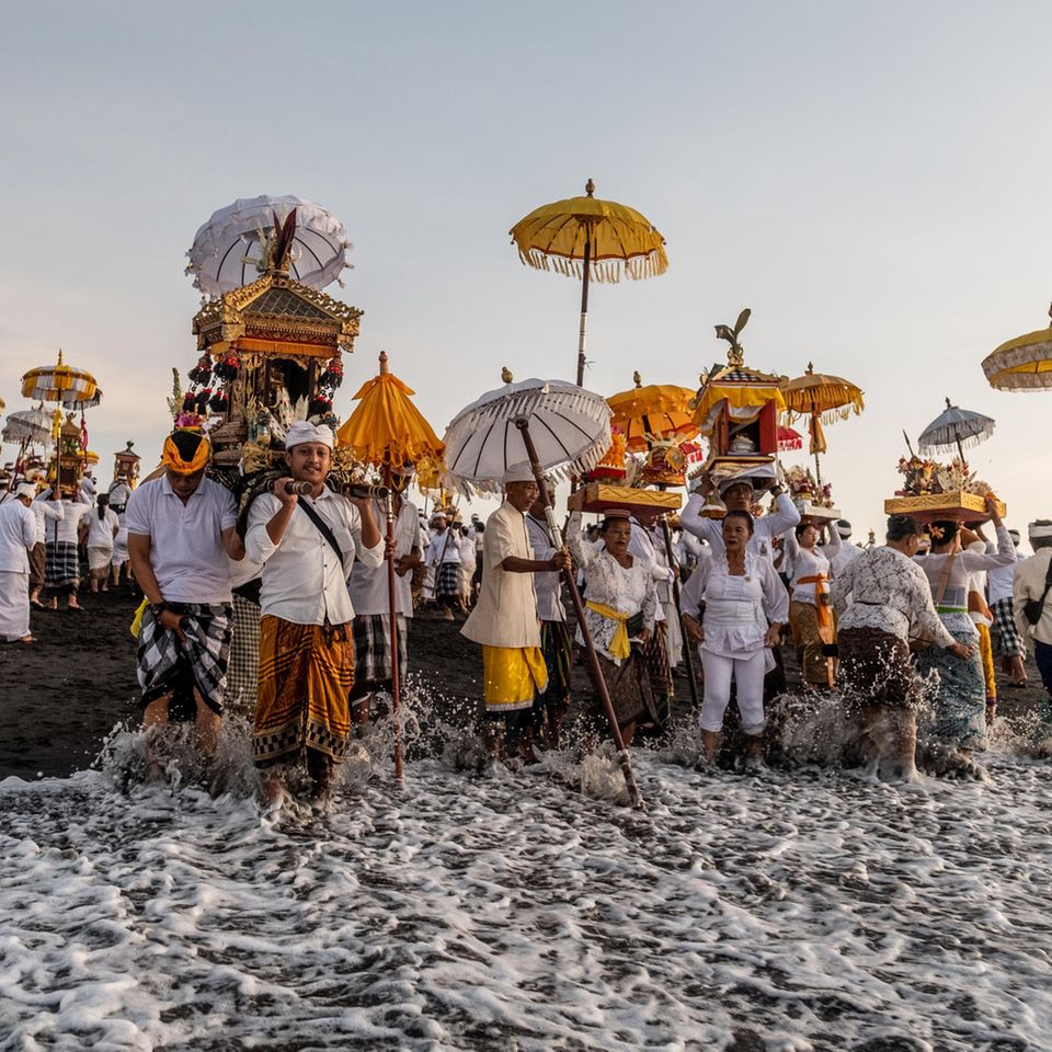 Gianyar Bali, Indonesien. Mit Masken, heiligen Bildnissen und rituellen Utensilien führen balinesische Hindus am Strand von Siyut eine Reinigungszeremonie durch. Die Menschen glauben, dass das Melasti-Ritual vor dem Nyepi-Tag, dem Tag der Stille, ein Muss ist, um die Seele und die Natur zu reinigen.