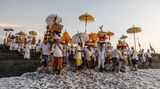 Gianyar Bali, Indonesien. Mit Masken, heiligen Bildnissen und rituellen Utensilien führen balinesische Hindus am Strand von Siyut eine Reinigungszeremonie durch. Die Menschen glauben, dass das Melasti-Ritual vor dem Nyepi-Tag, dem Tag der Stille, ein Muss ist, um die Seele und die Natur zu reinigen.