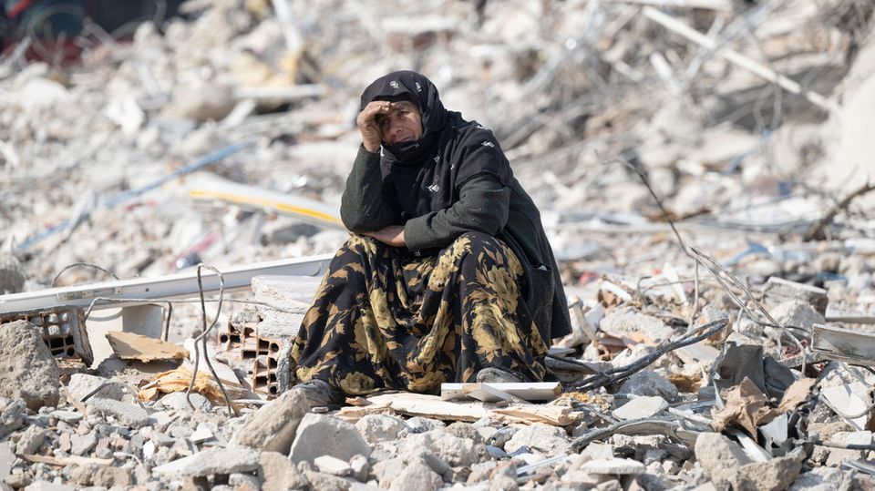 Antakya in der Türkei: Eine Frau sitzt zwischen den Trümmern und beobachtet die Bergung von Opfern des Erdbebens