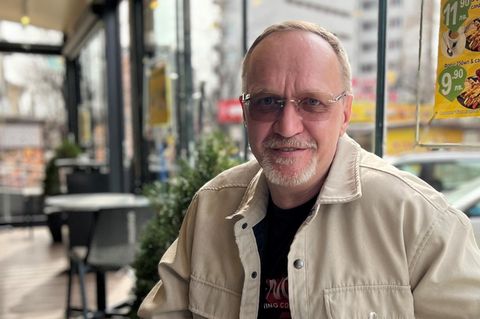 André Hoek sitzt an einem Tisch in einem Café vor ihm steht ein Glas mit Kaffee drin