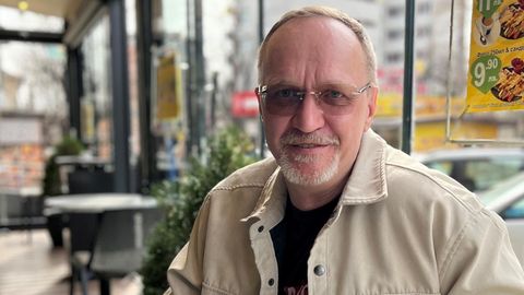 André Hoek sitzt an einem Tisch in einem Café vor ihm steht ein Glas mit Kaffee drin