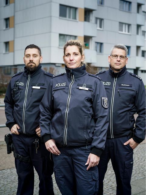 Drei Berliner Polizisten (zwei Männer und eine Frau) stehen vor einem Hochaus in Neukölln