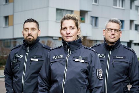 Drei Berliner Polizisten (zwei Männer und eine Frau) stehen vor einem Hochaus in Neukölln
