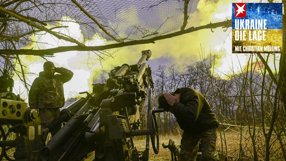 In der Ukraine halten sich zwei Soldaten die Ohren zu, während sie ein Geschütz abfeuern, das einen Feuerball ausstößt