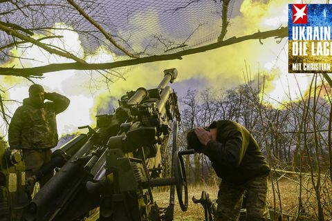 In der Ukraine halten sich zwei Soldaten die Ohren zu, während sie ein Geschütz abfeuern, das einen Feuerball ausstößt