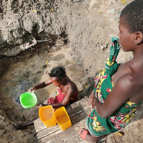 Eine Frau holt Wasser aus einer ungeschützten Quelle in Mosambik