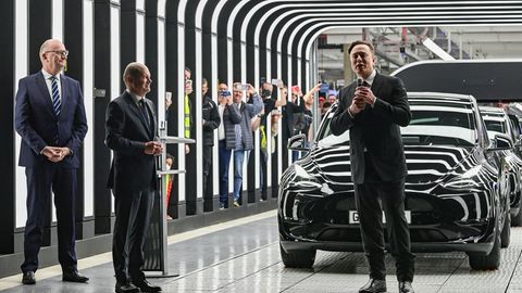 Tesla-Chef Elon Musk steht vor mehreren Autos. Neben ihm steht Brandenburgs Ministerpräsident Dietmar Woidke und Olaf Scholz