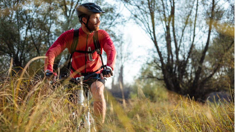 Radmode für Männer 2023: Mountainbike im hohen Gras am Waldrand