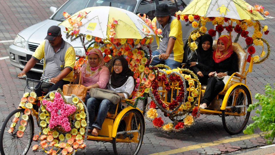Zwei mit Blumen geschmückte Rikschas fahren Frauen durch Malakka