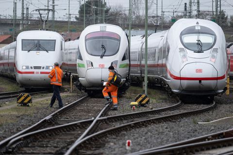 Auf einem Rangierbahnhof gehen zwei orange gekleidete Männer vor stehenden ICE-Loks über die Gleise