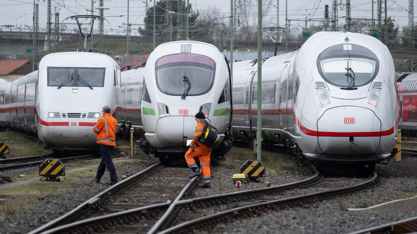 Auf einem Rangierbahnhof gehen zwei orange gekleidete Männer vor stehenden ICE-Loks über die Gleise