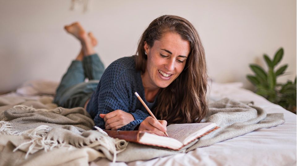 Frau liegt auf dem Bett und schreibt Tagebuch