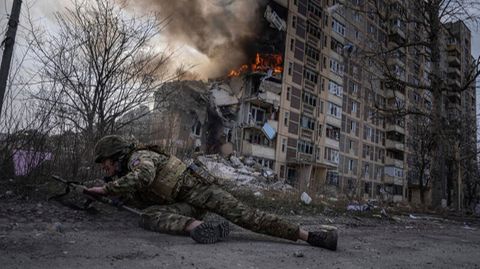 Ein ukrainischer Soldat geht vor einem brennenden Gebäude in Awdijiwka in Deckung