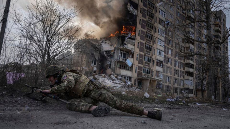 Ein ukrainischer Soldat geht vor einem brennenden Gebäude in Awdijiwka in Deckung