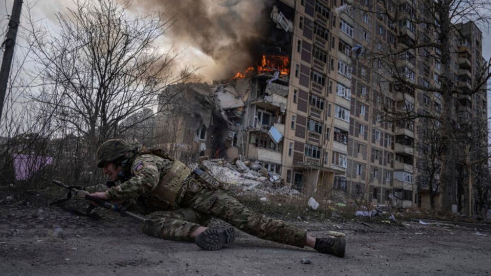 Ein ukrainischer Soldat geht , der vor einem brennenden Gebäude in Awdijiwka in Deckung (Archivbild)