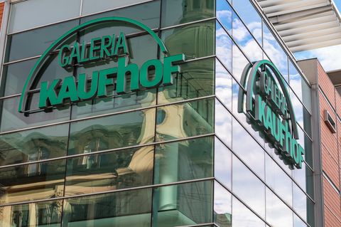 An einer verspiegelten Glasfassade hängt das grüne Logo von Galeria Kaufhof