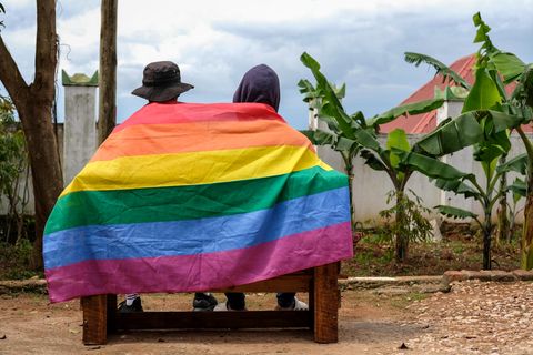 Zwei Personen in Uganda sind von hinten auf einer Bank zu sehen, ihre Rücken bedeckt von einer Regenbogen-Flagge