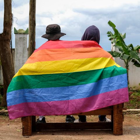Zwei Personen in Uganda sind von hinten auf einer Bank zu sehen, ihre Rücken bedeckt von einer Regenbogen-Flagge