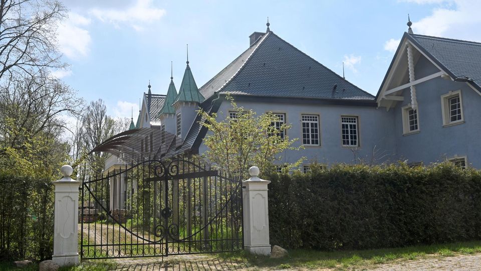 Ein Schlossgebäude hinter einer Hecke und einem Gittertor