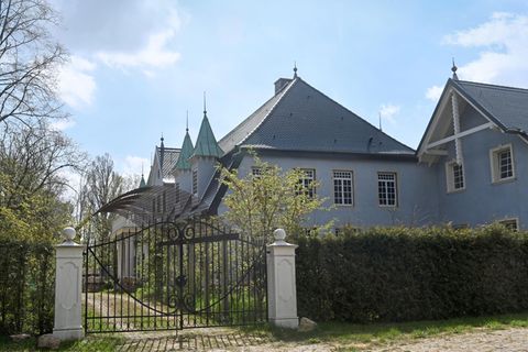 Ein Schlossgebäude hinter einer Hecke und einem Gittertor