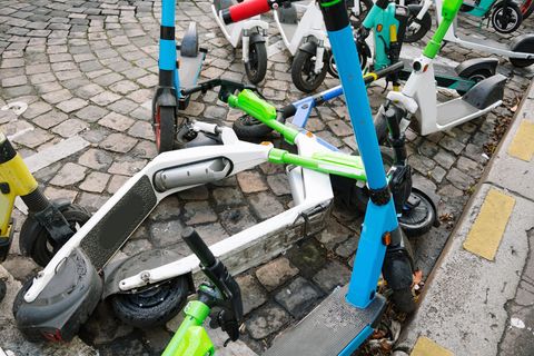Auf Kopfsteinpflaster stehen und liegen unterschiedlich lackierte E-Roller