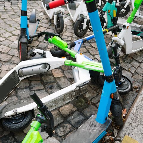 Auf Kopfsteinpflaster stehen und liegen unterschiedlich lackierte E-Roller