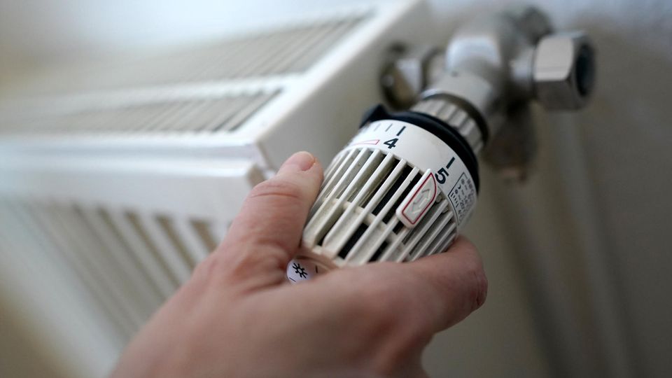 Eine Frau dreht am Thermostat einer Heizung